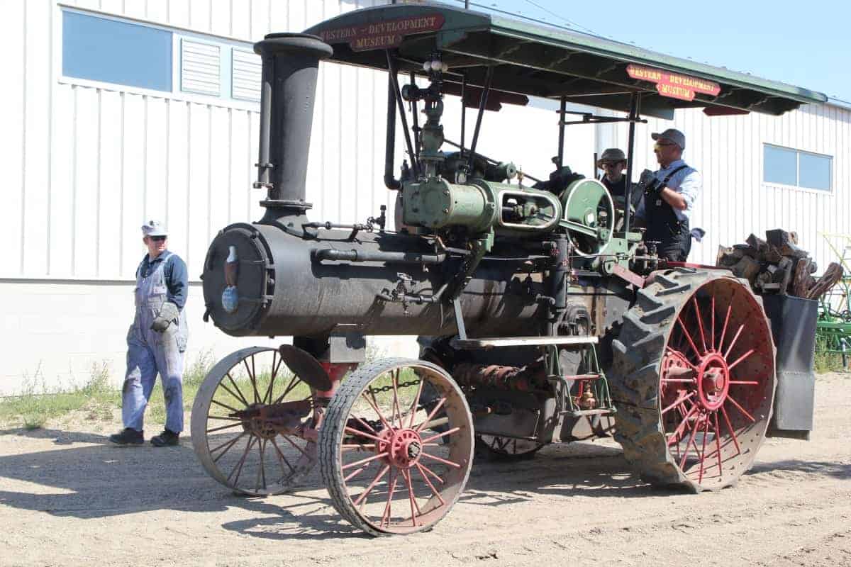 Two men operate the 35 HP Case steam traction engine while 1 man walks alongside