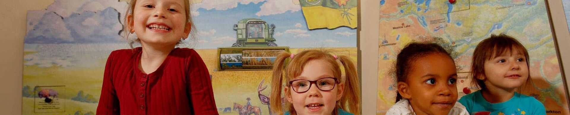 Four smiling children in front of a pictures showing a threshing machine on a wheat field.
