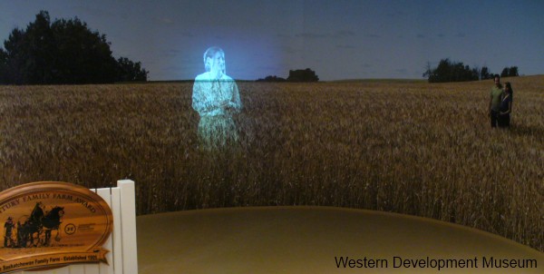 Projection of a woman gazes at an image of a wheat field and reminisce's about her family's agriculture background and future.
