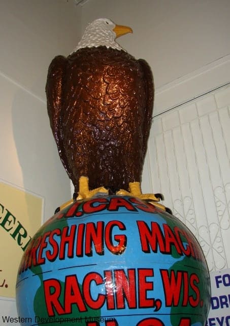 Large eagle sitting on top of a globe. Wording reads J.I. Case Threshing Machine. Racine Wis, U.S.A.