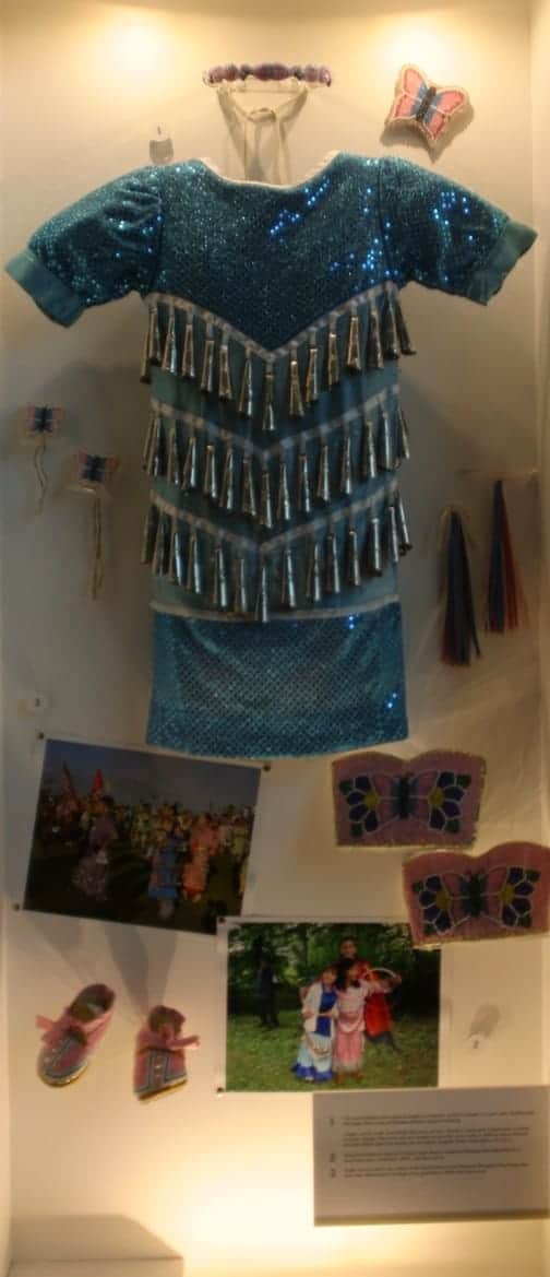 Photo of blue jingle dress with other photos , shoes and other items on display.