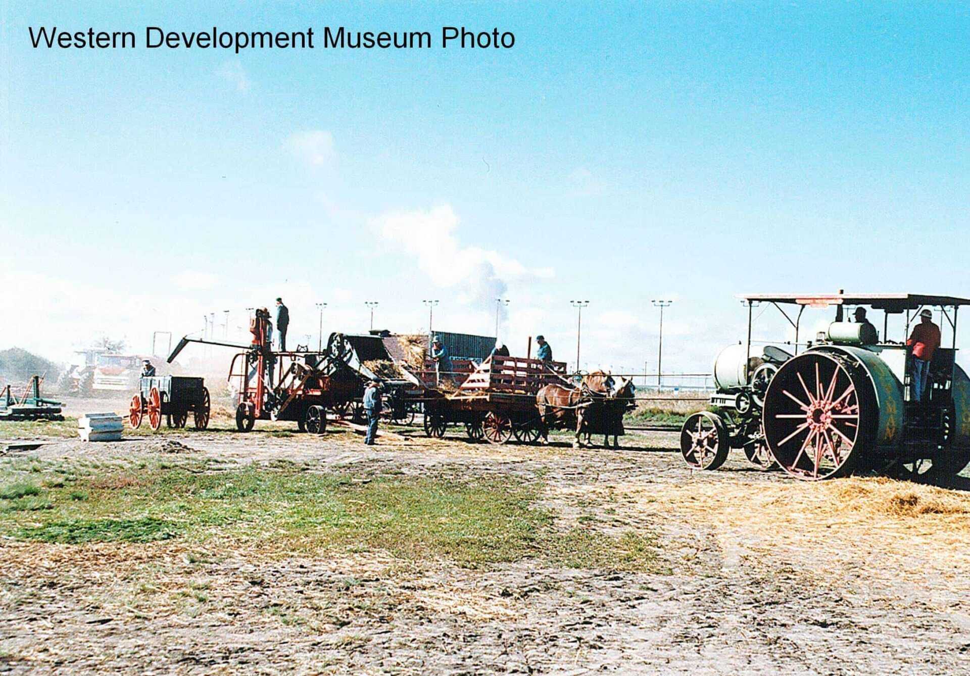 Re-enacted circa 1920s agriculture scene: Grain harvest scene, featuring a gas tractor, threshing machine, horse drawn bundle wagon