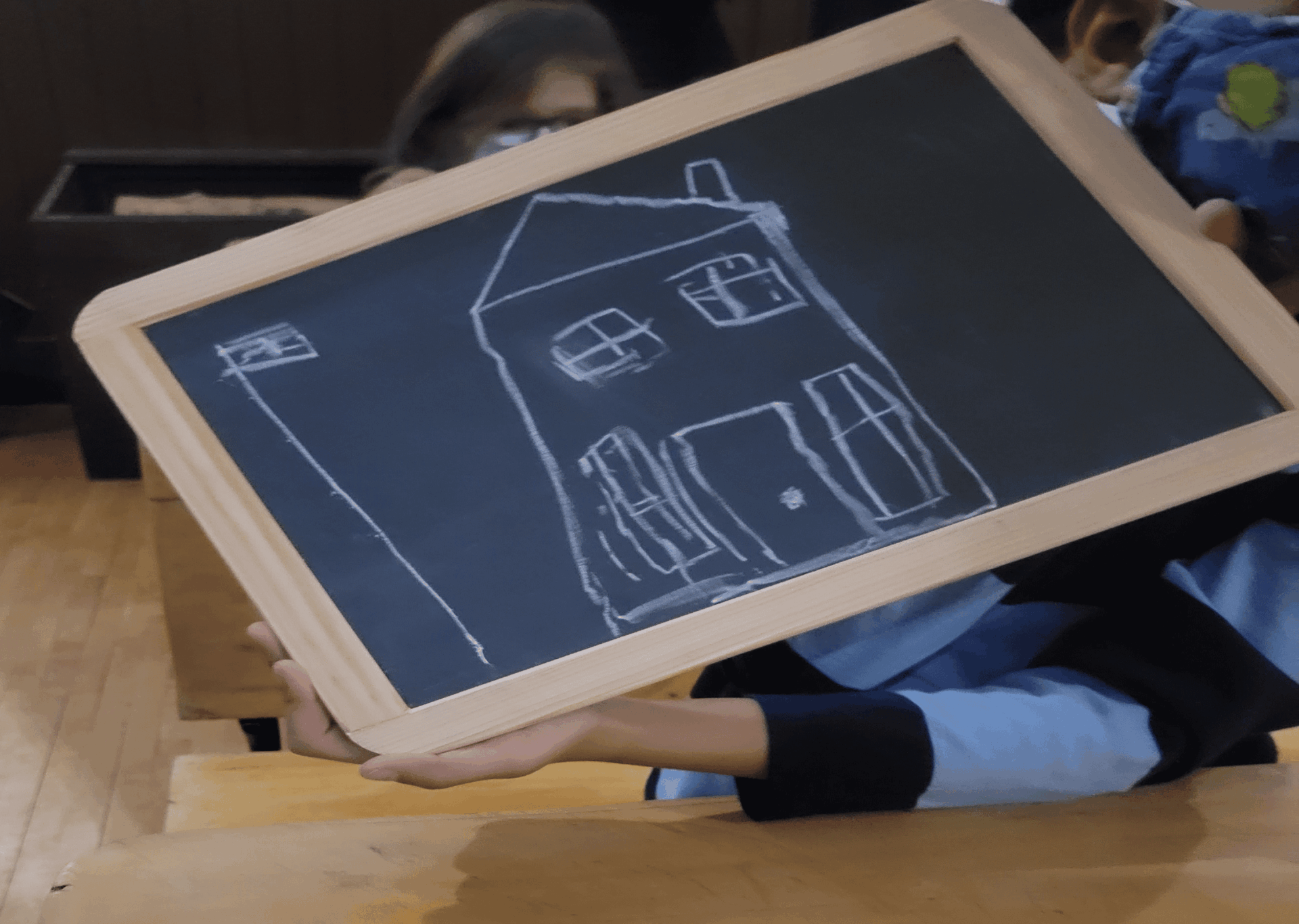 Slate board with child's drawing of a small school house with a flag flying on a pole beside it