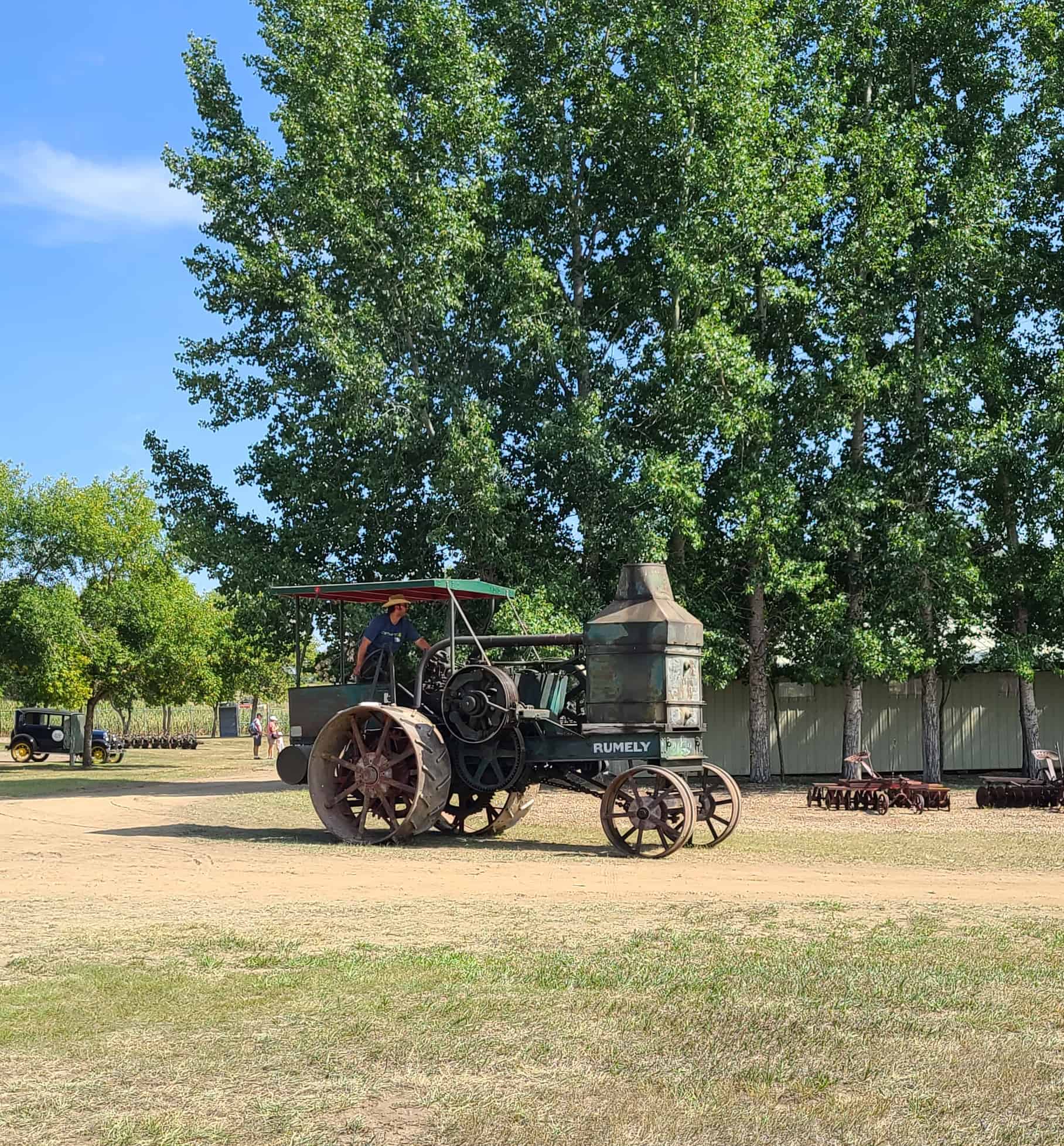 Antique Rumley tractor in front of tall green trees