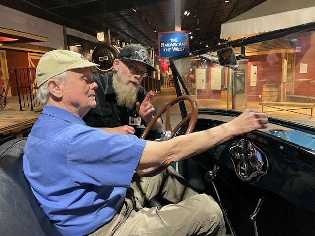 Man sits in the driver's seat of a McLaughlin car. Another man looks over his shoulder.