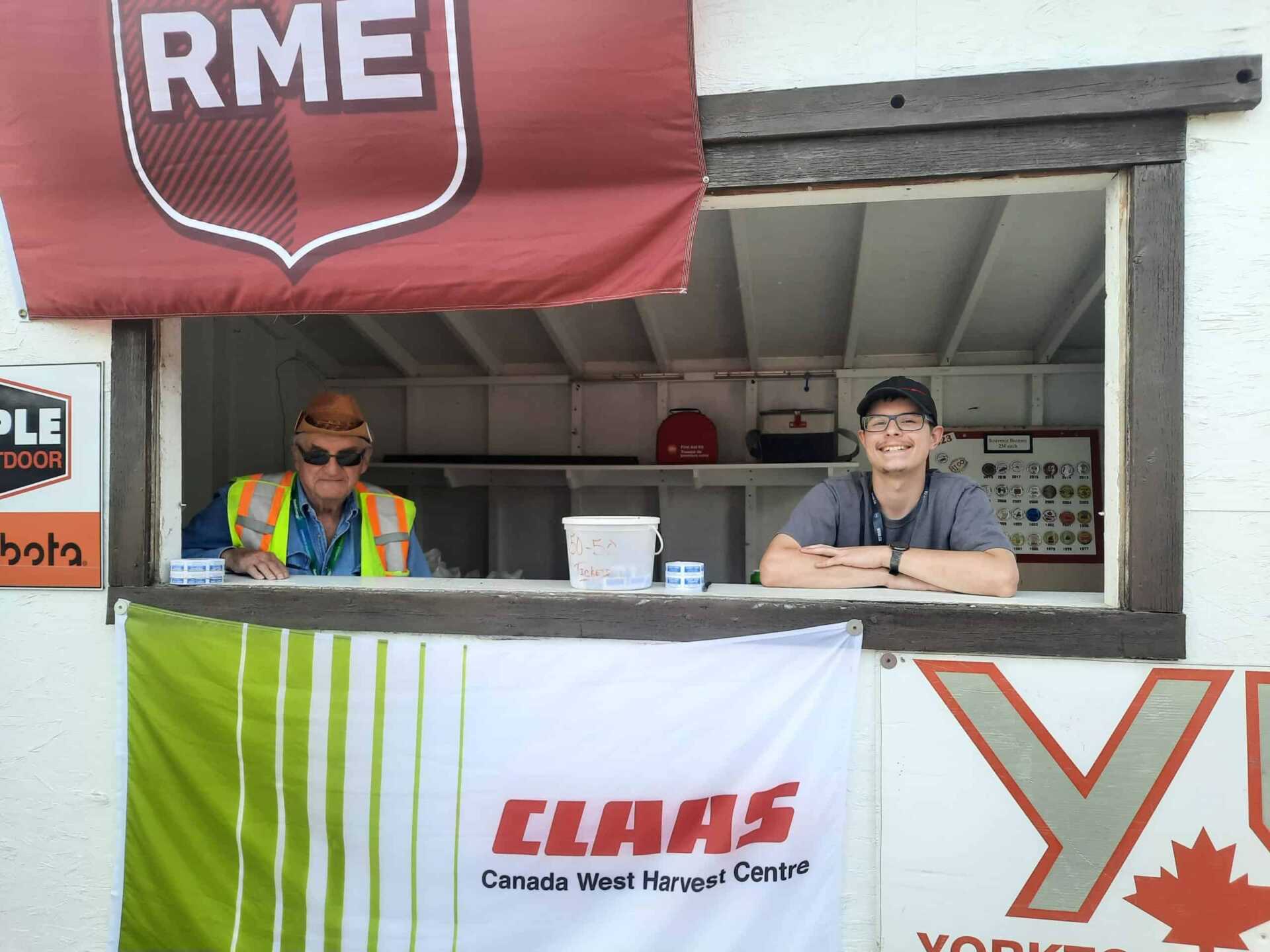 Two volunteers look out from a booth where they are selling 50/50 tickets