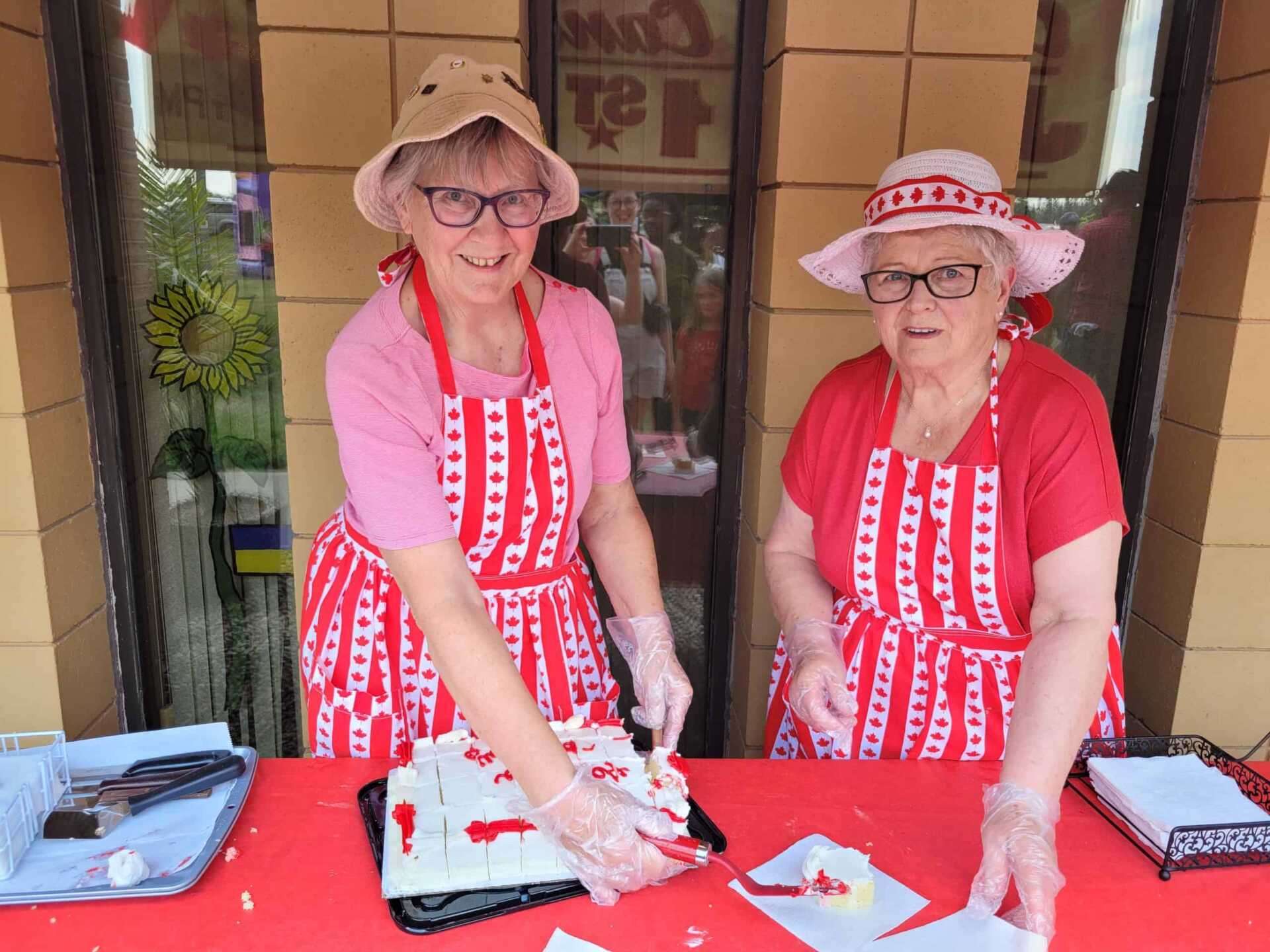 Two women in red and white outfits hand out Canada Day themed cake