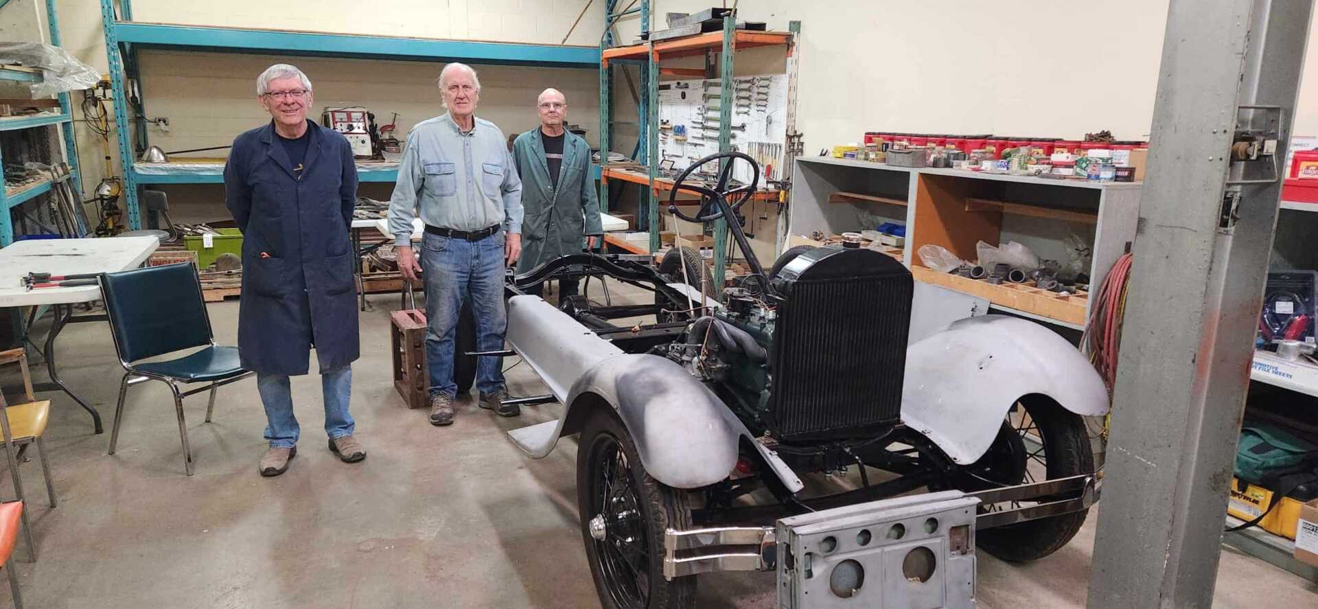 3 men stand beside a model A Ford frame