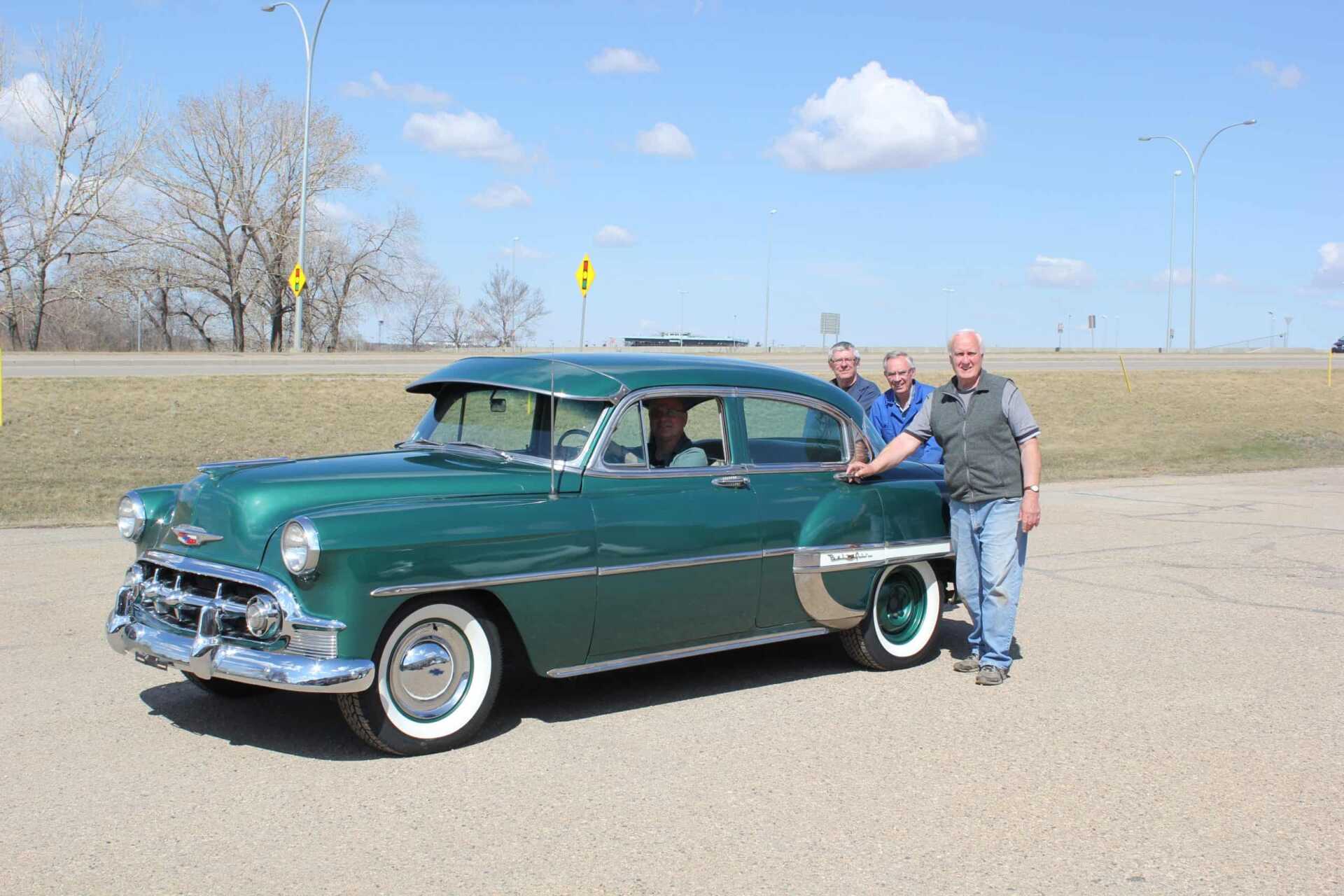 Three men stand beside restored Chevy car