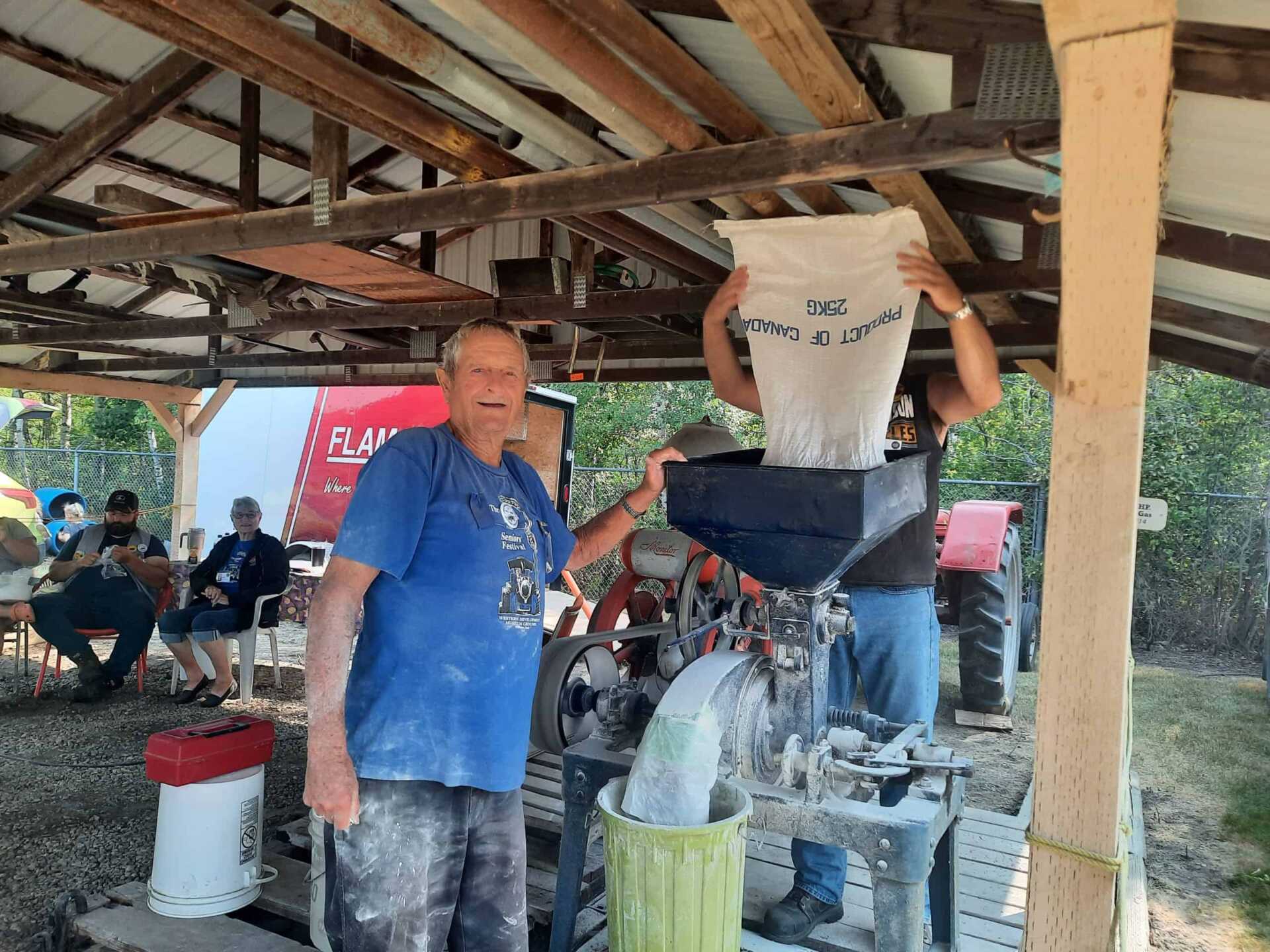 Man stands beside hand cranked wheat grinder
