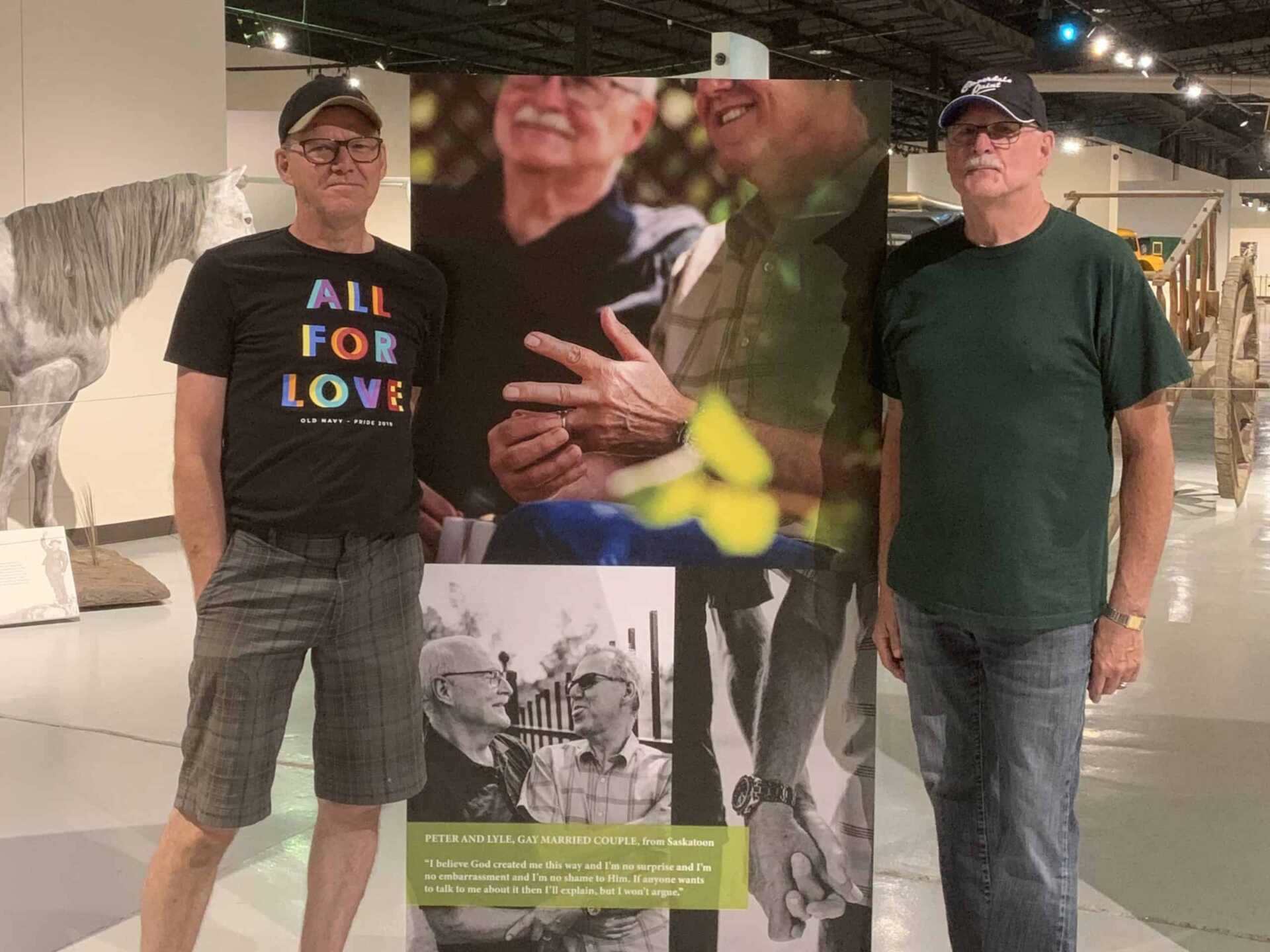 A married couple, Peter and Lyle, stand beside a banner promoting 2SLGBTQ+ rights.