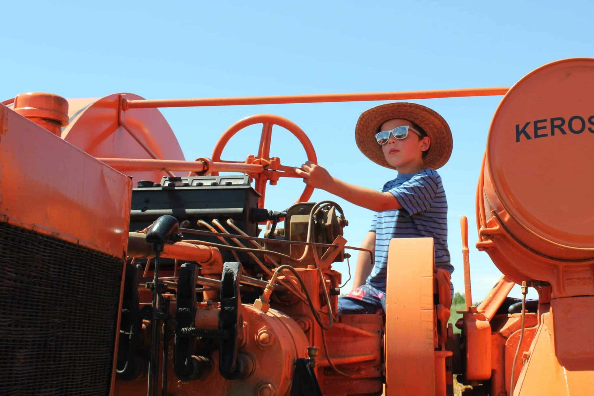 A boy wearing sunglasses sits on an orange Happy Farmer tractor.