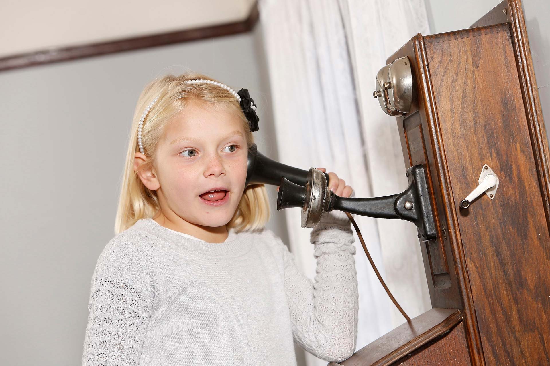 Young girl tries out a 1920s wall telephone