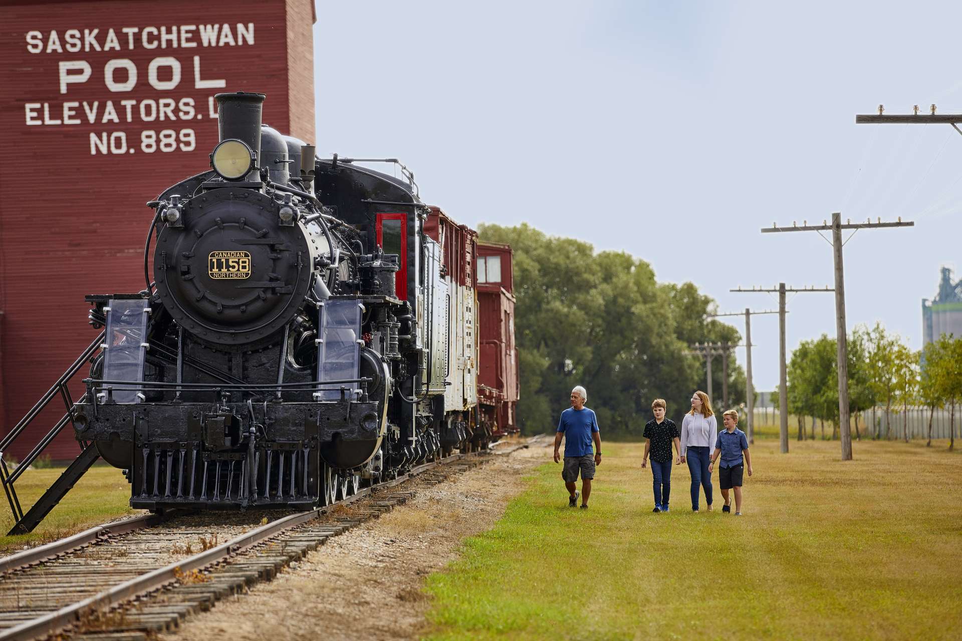 A family walks alongside a train and grain elevator.