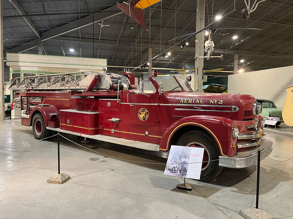 A red ladder fire truck with an open driver's cab from the 1950s.